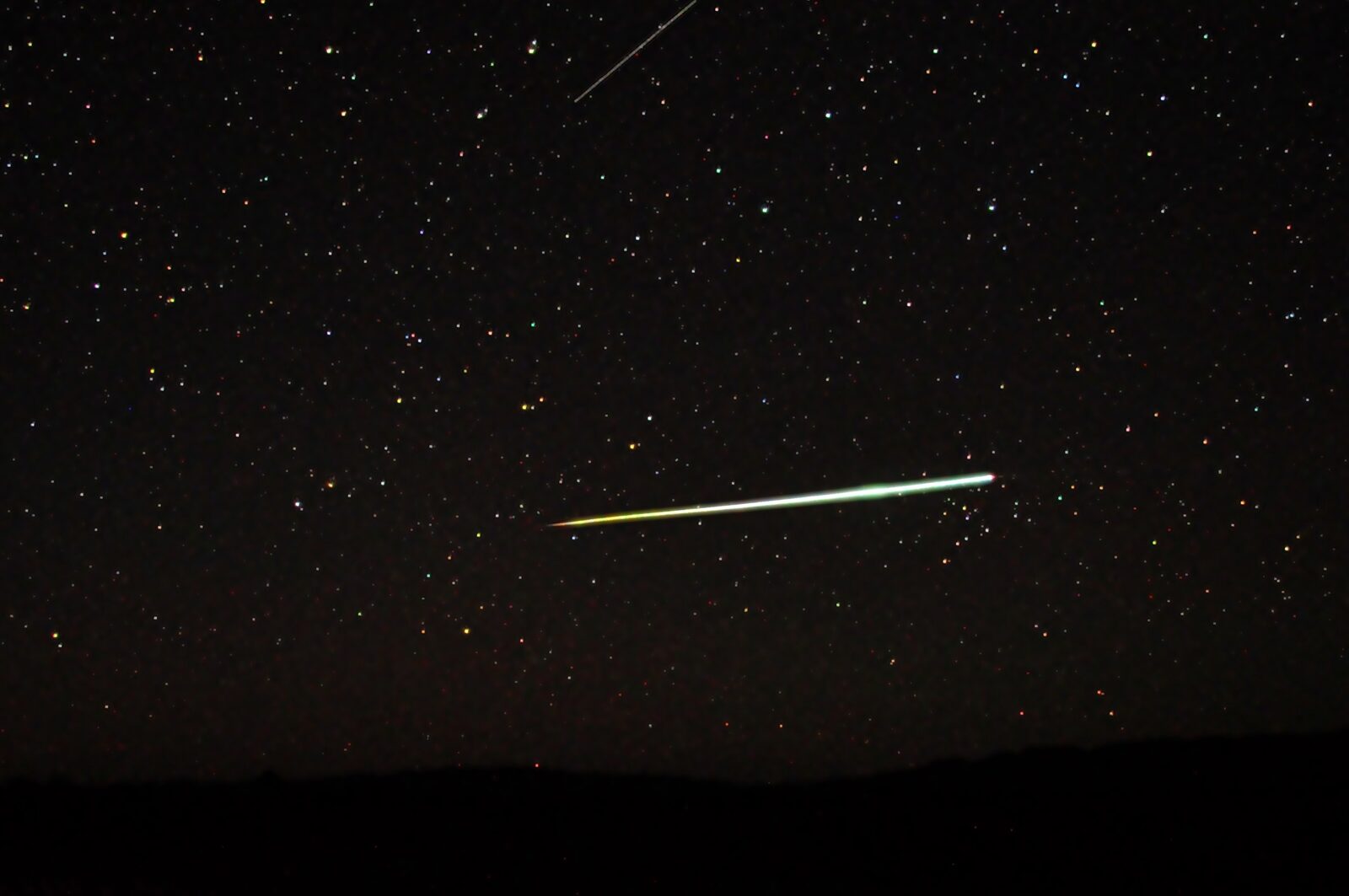 Long-exposure night photograph of a bright bolide fireball streaking across a starry sky above a dark horizon