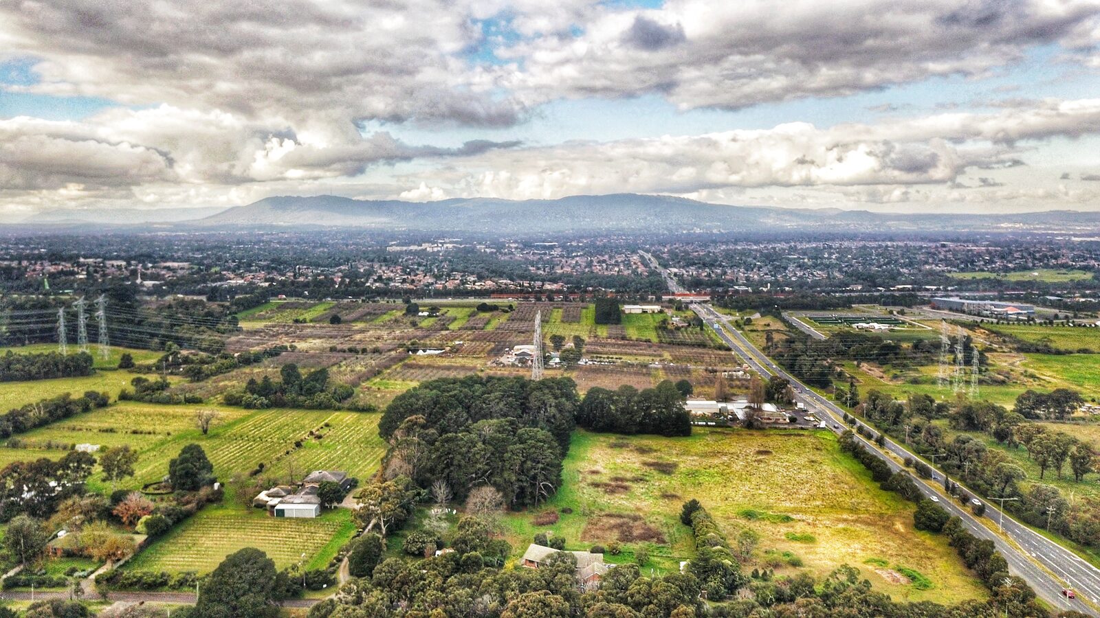 Aerial photograph looking east across suburban rooftops and treed slopes toward the Dandenong Ranges in Victoria, Australia