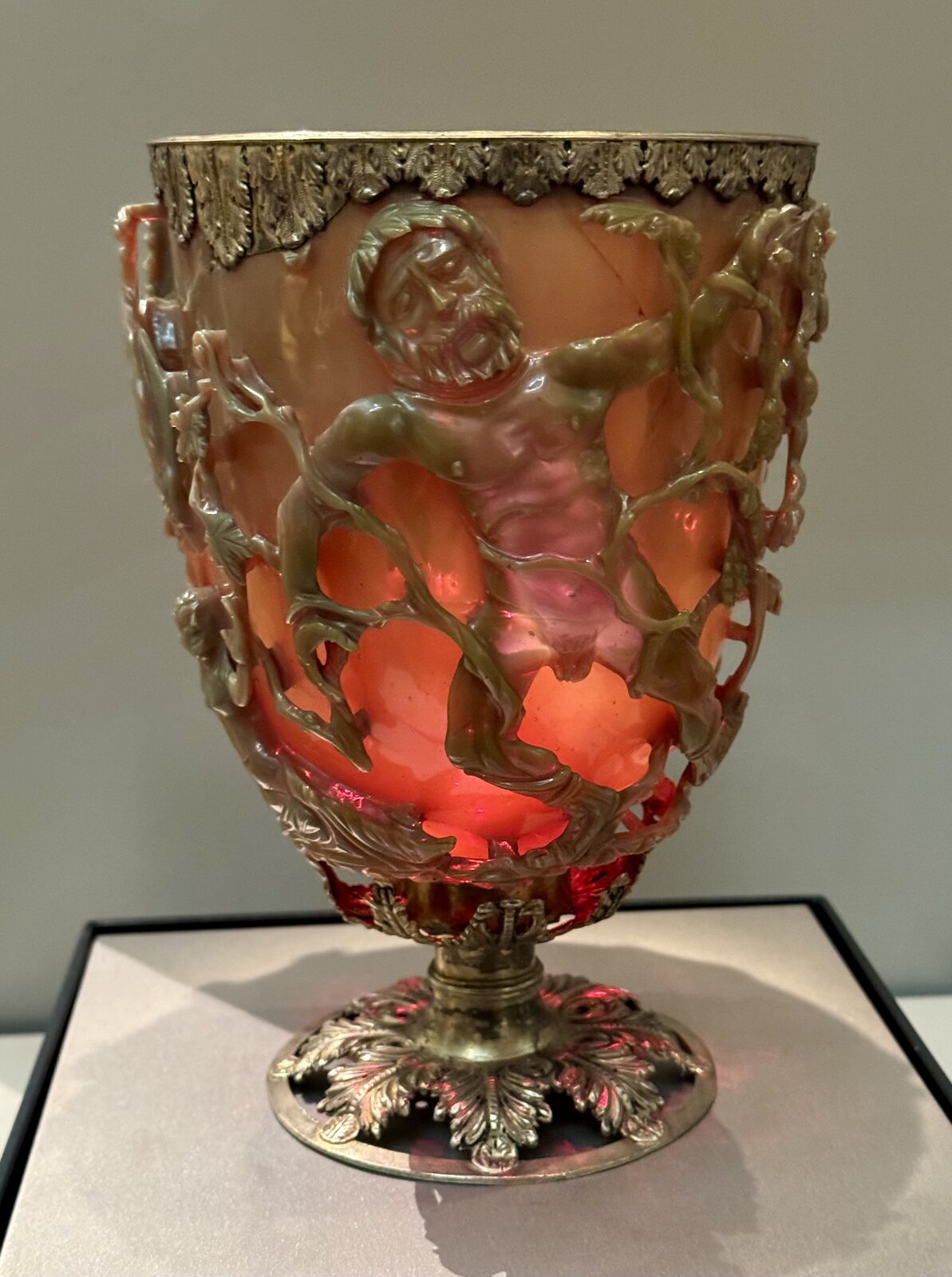 Front view of the Lycurgus Cup appearing opaque jade-green in reflected light, with carved openwork figures standing proud of the vessel wall