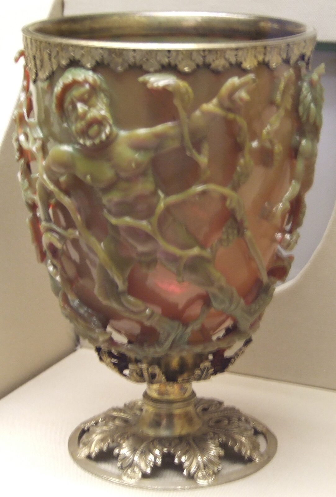 The Lycurgus Cup photographed in its display case at the British Museum, showing the green reflected-light appearance and the depth of the undercut carving