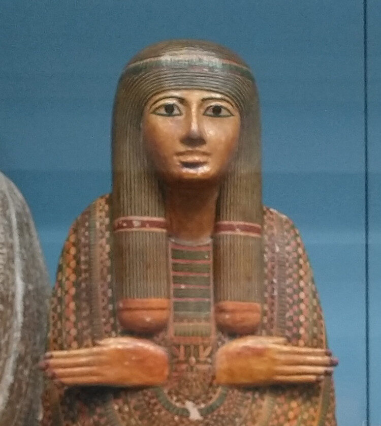 Painted wooden Egyptian mummy-board of an unidentified woman, with protruding hands and painted plaster detail, displayed in a glass case at the British Museum